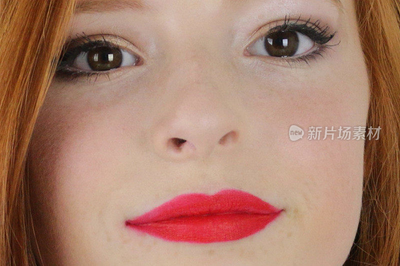 这张特写照片是一个14 / 15岁的红发少女，皮肤苍白，脸上有雀斑，坐在卧室里测试她嘴唇上亮红色的口红，嘴唇噘起自然的脸部妆容